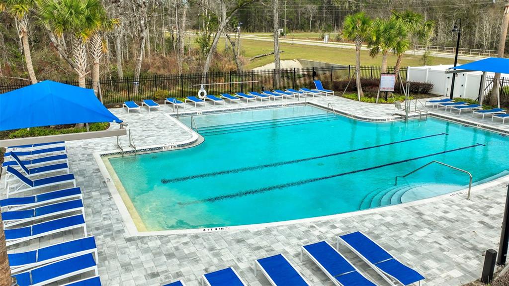 An outdoor swimming pool with lounge chairs and blue shade structures on a paved deck — 3167 GADWALL ROAD, ORANGE PARK, FL