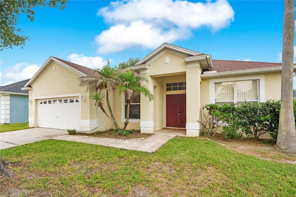 A single-story house with a beige stucco exterior, a two-car garage, and a red front door — 1019 BRIDGEWAY BOULEVARD, ORLANDO, FL