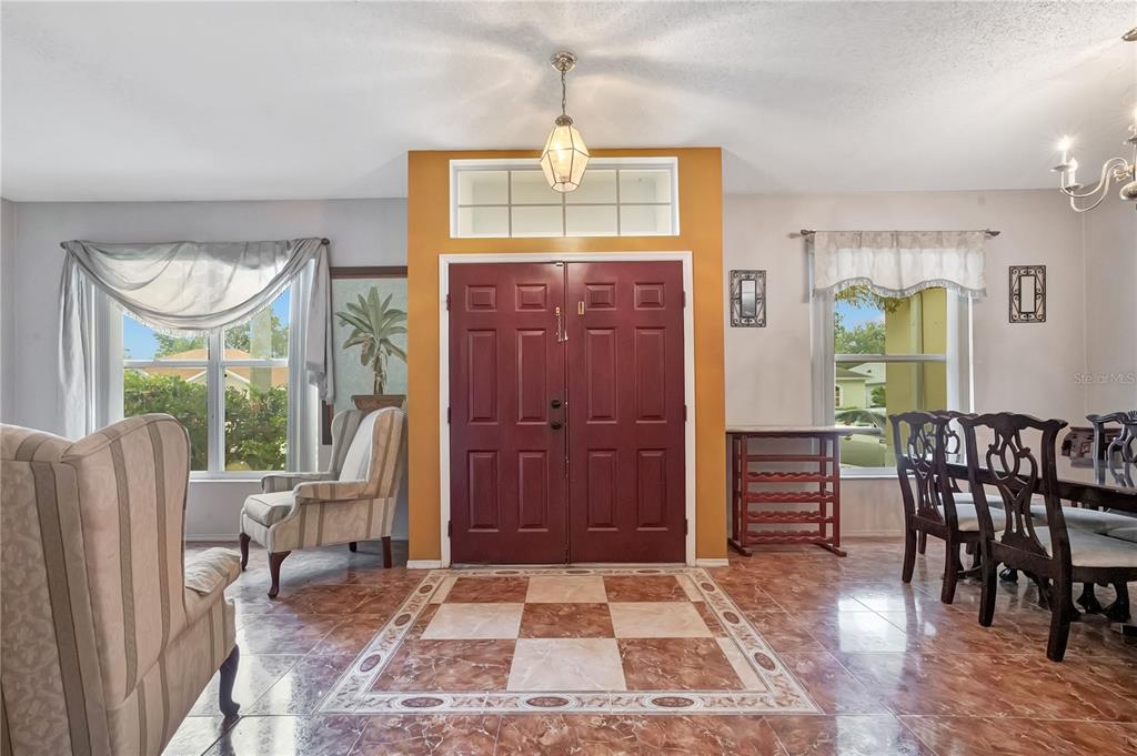 A foyer with a checkerboard tile floor, double red doors, and a dining area — 1019 BRIDGEWAY BOULEVARD, ORLANDO, FL