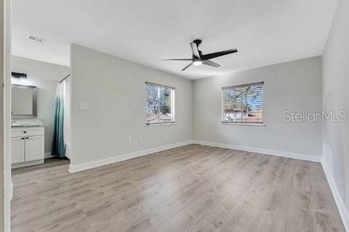 A bedroom with light gray walls, wood-look flooring, a ceiling fan, and an attached bathroom — 196 W SABAL PALM PLACE UNIT 196, LONGWOOD, FL