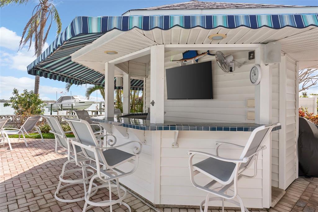 A swimming pool and patio overlook a waterfront dock with a boat and jet ski — 11445 9TH STREET E, TREASURE ISLAND, FL