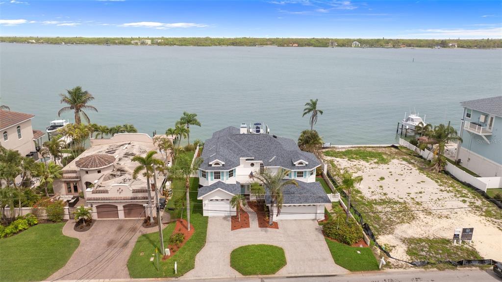 A two-story white house with teal shutters features two garages and palm trees outside — 11445 9TH STREET E, TREASURE ISLAND, FL