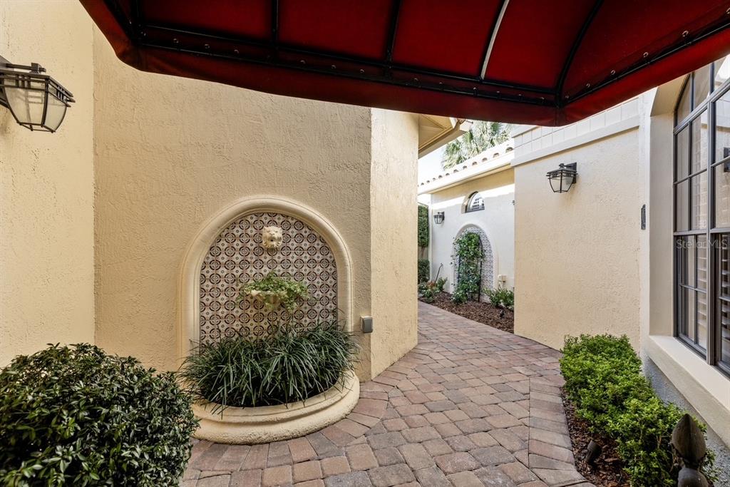 A paved walkway leads past a decorative wall fountain toward a courtyard entrance — 2428 VIA GENOVA, APOPKA, FL