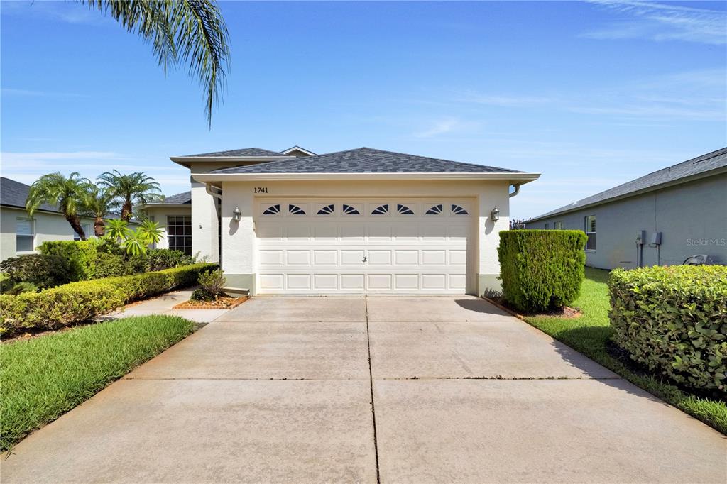 A single-story house features a two-car garage, a concrete driveway, and manicured landscaping — 1741 ARBOR KNOLL LOOP, TRINITY, FL