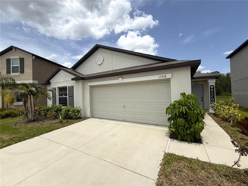 A single-story house with a beige stucco exterior, a two-car garage, and a concrete driveway — 15516 MILLER CREEK DRIVE, SUN CITY CENTER, FL
