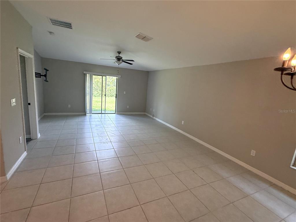 An empty living room features light-colored tile flooring, beige walls, and a sliding glass door — 15516 MILLER CREEK DRIVE, SUN CITY CENTER, FL
