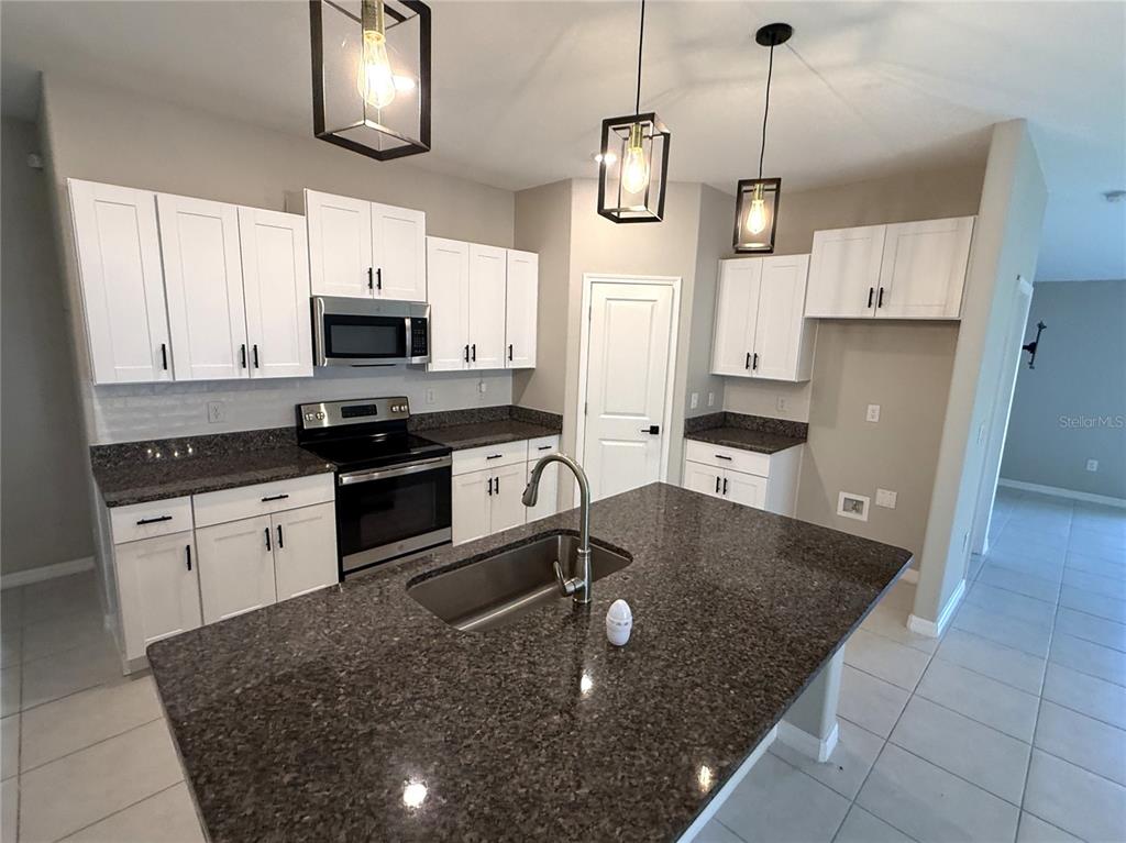 A kitchen features white cabinetry, dark granite countertops, a center island, and three pendant lights — 15516 MILLER CREEK DRIVE, SUN CITY CENTER, FL