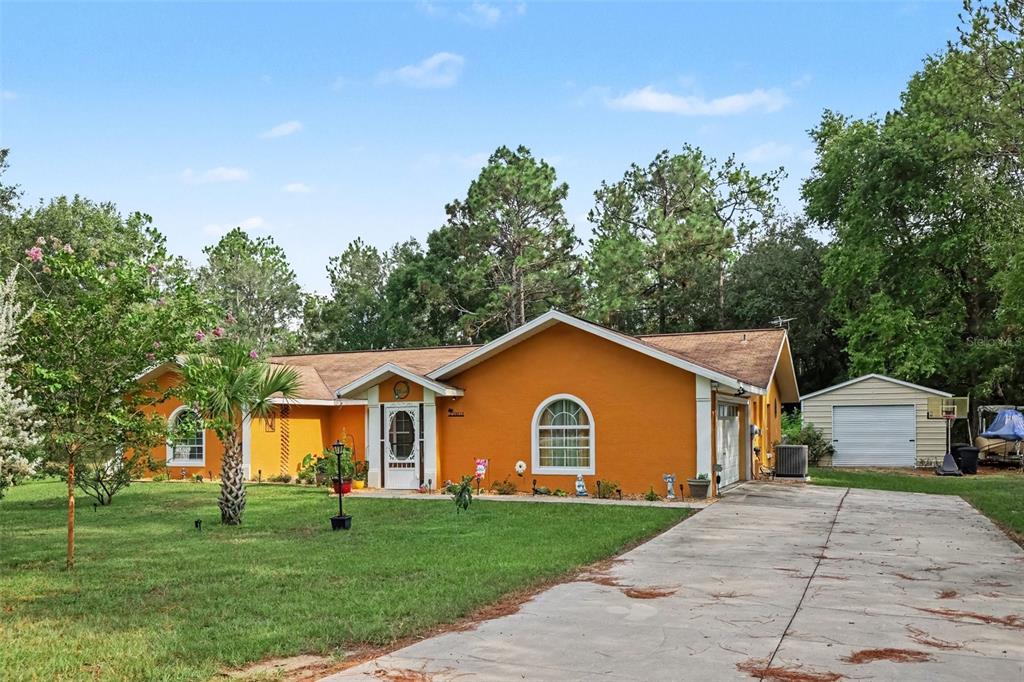 A single-story orange house with a concrete driveway and a detached shed in the yard — 18018 SW 68TH LOOP, DUNNELLON, FL