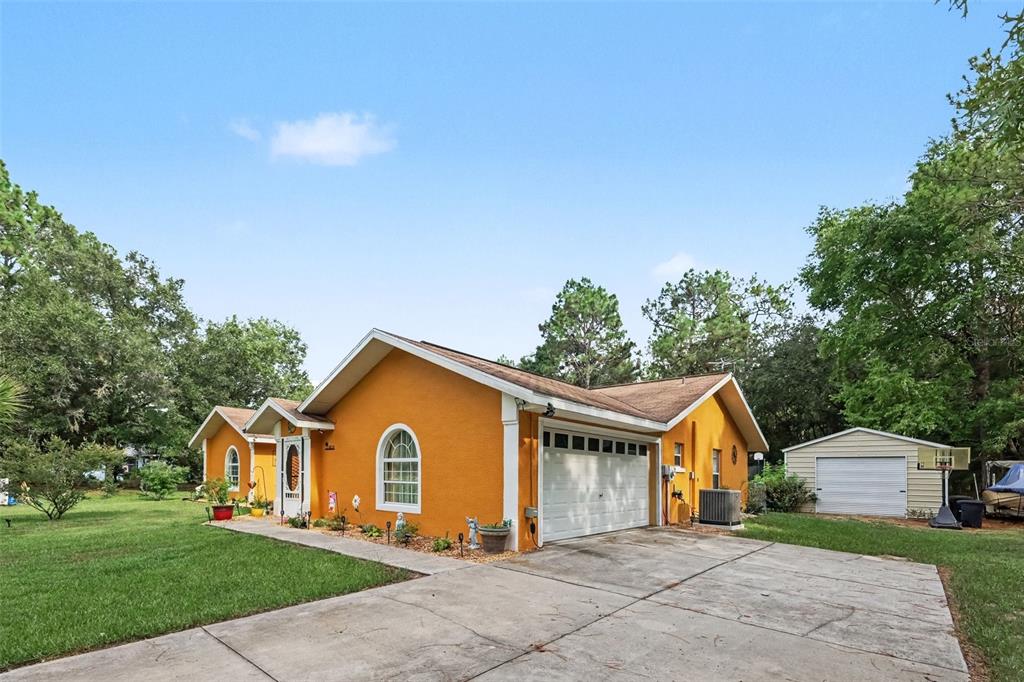 A bright orange single-story house with a white garage door and a detached shed — 18018 SW 68TH LOOP, DUNNELLON, FL