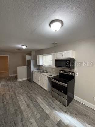 A kitchen features stainless steel appliances, white cabinets, and gray wood-look flooring — 225 1ST STREET, WINTER GARDEN, FL
