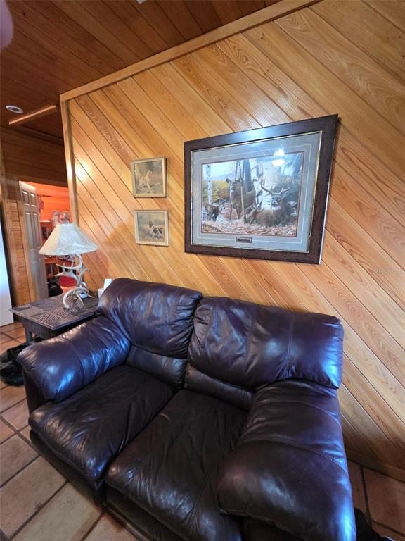 A living room features a dark leather loveseat, diagonal wood-paneled walls, and nature-themed artwork — 1106 FOX HUNTER RD, PERRY, FL