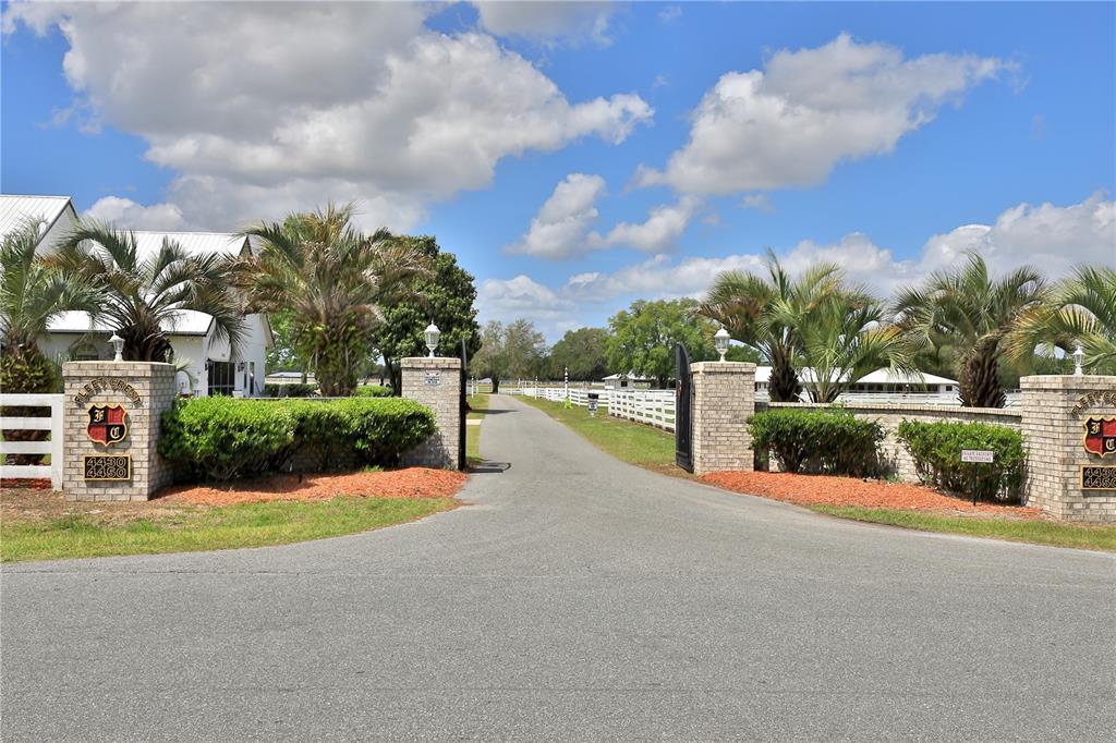A paved driveway leads through a brick gated entrance to a property with white fencing — 4450 SE 216TH AVENUE, MORRISTON, FL