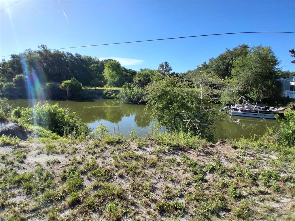 A grassy bank overlooks a calm canal with a pontoon boat docked near the shore — 4366 WHITING WAY, EDGEWATER, FL