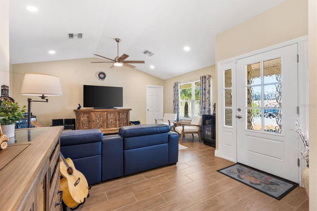 A living room features a blue sofa, wood-look tile flooring, a vaulted ceiling, and an entryway — 1026 SMYRNA STREET, THE VILLAGES, FL