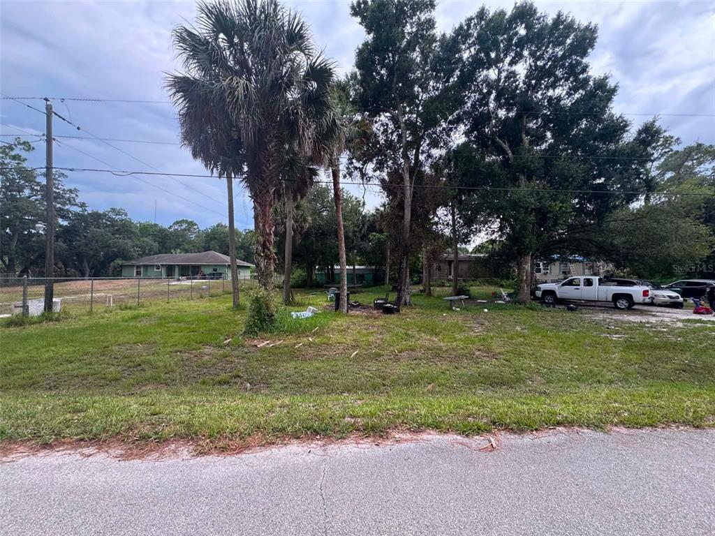A grassy vacant lot features several mature trees, a palm tree, and a chain-link fence — 6702 NE 1ST STREET, OKEECHOBEE, FL