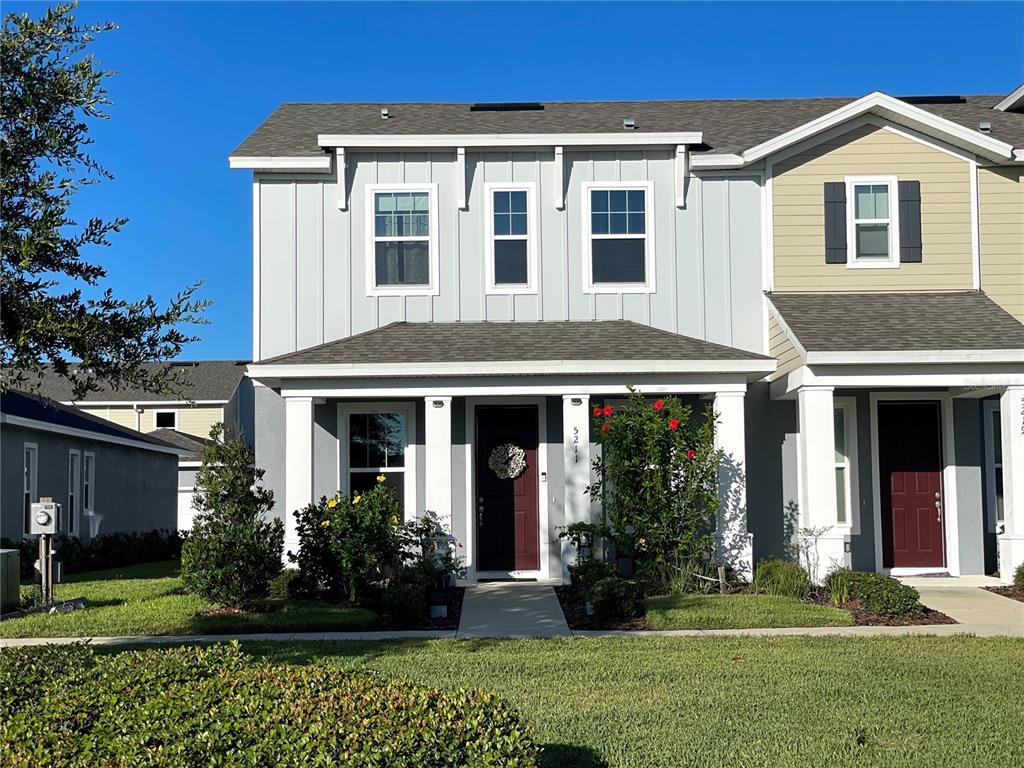 A two-story townhouse with a covered front porch, gray siding, and a dark red door — 5211 AVALON PARK BOULEVARD, WESLEY CHAPEL, FL
