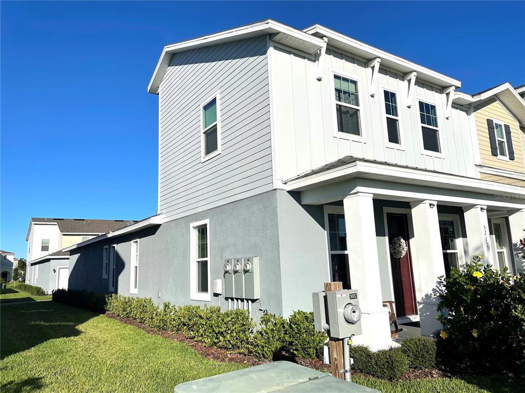 The exterior of a two-story residential building features gray siding, a front porch, and landscaping — 5211 AVALON PARK BOULEVARD, WESLEY CHAPEL, FL
