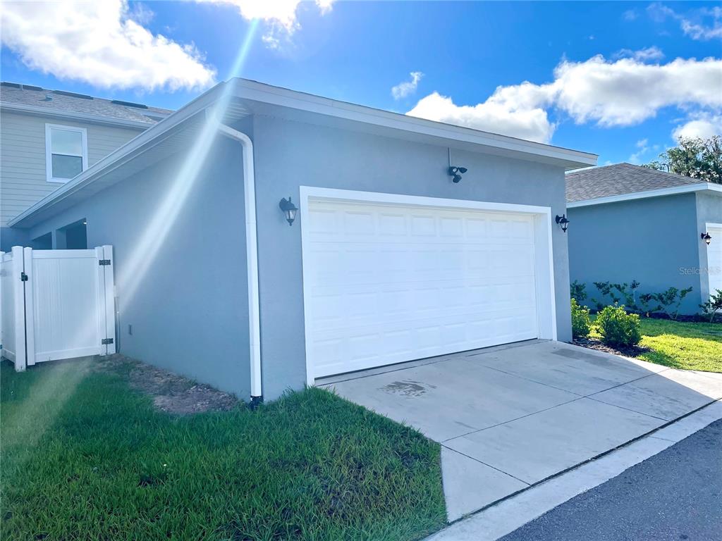 A blue house exterior features a white two-car garage door and a white side gate — 5211 AVALON PARK BOULEVARD, WESLEY CHAPEL, FL