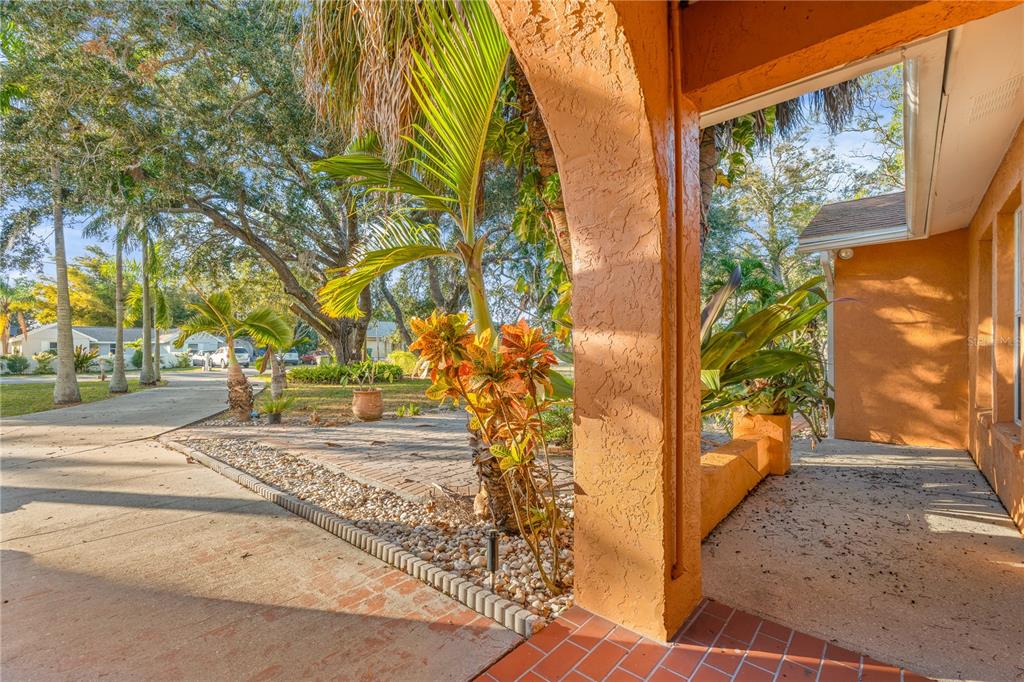 A view from a covered porch looking out toward a driveway, palm trees, and landscaping — 619 29TH STREET E, BRADENTON, FL
