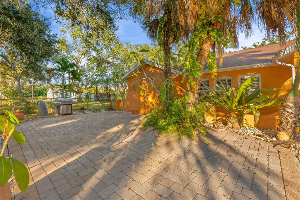 A paved patio sits beside an orange house with tropical landscaping and a backyard grill — 619 29TH STREET E, BRADENTON, FL