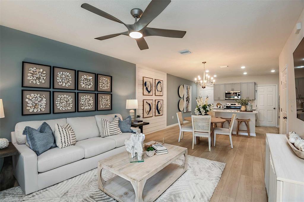A living room and dining area feature light wood floors, a blue accent wall, and coastal decor — 9885 PELICAN COAST DRIVE, DADE CITY, FL