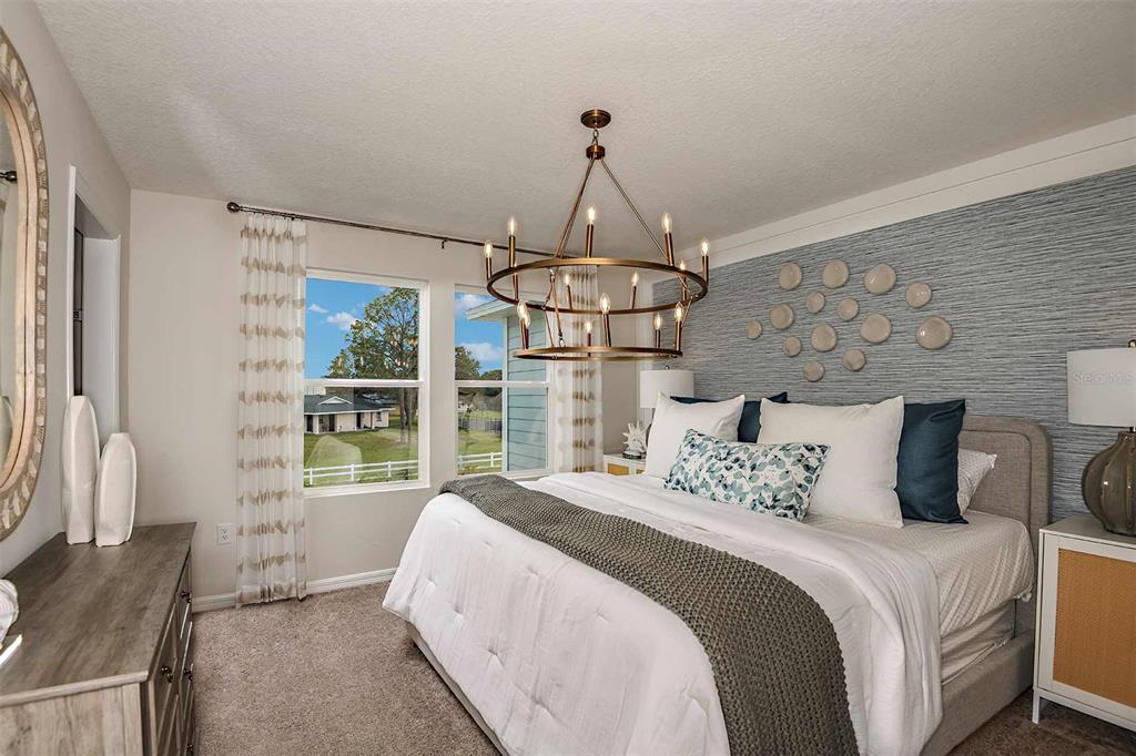 A bedroom features a bed with white bedding, a textured blue accent wall, and a chandelier — 9885 PELICAN COAST DRIVE, DADE CITY, FL