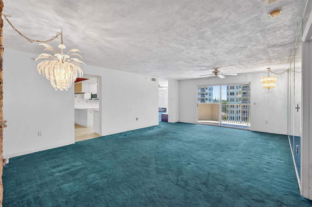 A living room with teal carpeting, a palm-shaped chandelier, and a sliding glass balcony door — 1 JOHN ANDERSON DRIVE UNIT 5150, ORMOND BEACH, FL