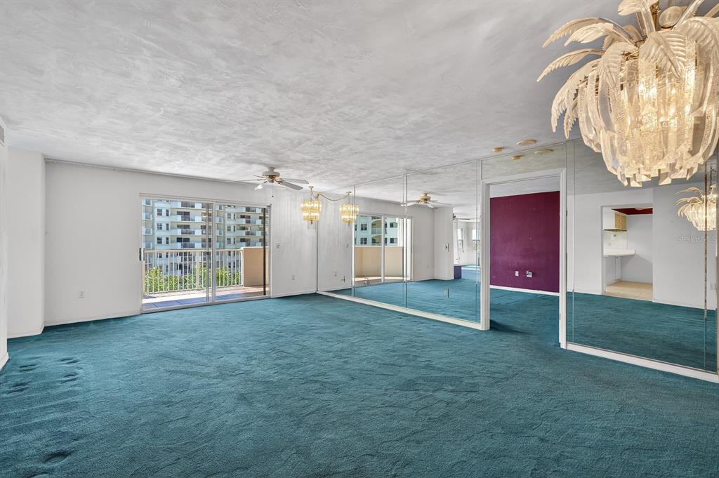 A living room with teal carpeting, mirrored walls, a palm-shaped chandelier, and a balcony view — 1 JOHN ANDERSON DRIVE UNIT 5150, ORMOND BEACH, FL