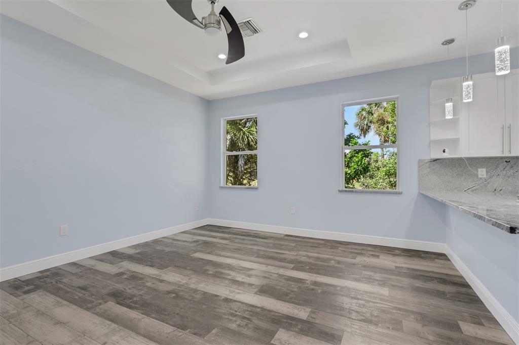 An empty room with light blue walls, wood-look flooring, and a granite-topped kitchen counter — 2977 4TH AVENUE SE, NAPLES, FL