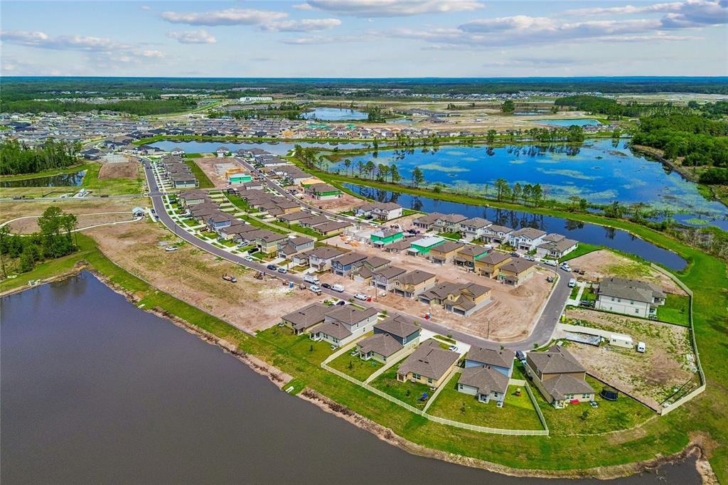 An aerial view shows a suburban neighborhood under construction with houses bordering a large lake — 7915 PAINTED SKY PLACE, LAND O LAKES, FL