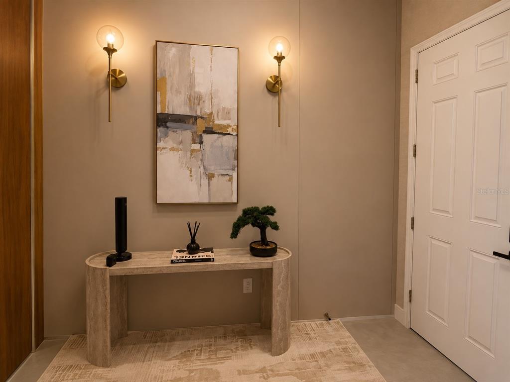 A modern entryway features a stone console table, abstract wall art, and two gold wall sconces — 12989 WESTSIDE VILLAGE LOOP, WINDERMERE, FL