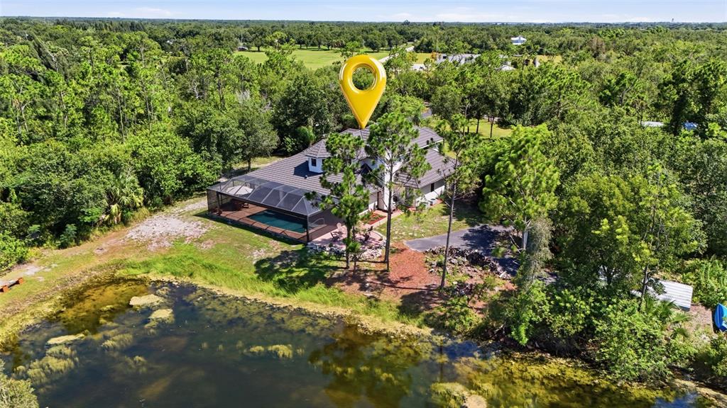 An aerial view shows a house with a pool and screened lanai beside a pond — 6000 CLEVELAND DRIVE, PUNTA GORDA, FL