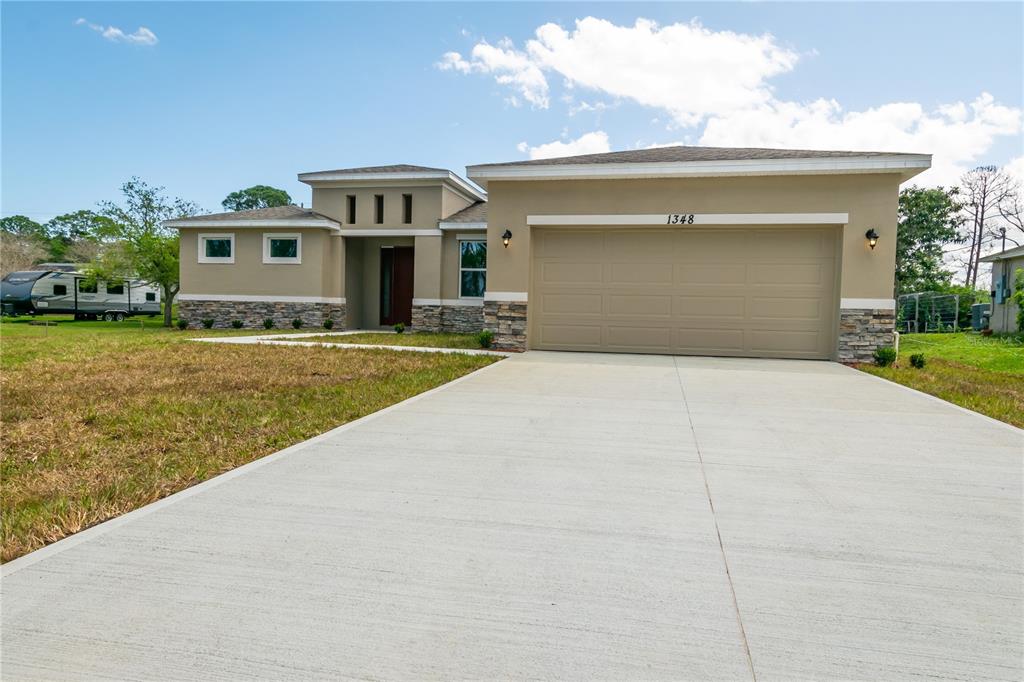A modern single-story house with a tan stucco exterior, stone accents, and a concrete driveway — 1348 PALAU STREET SE, PALM BAY, FL