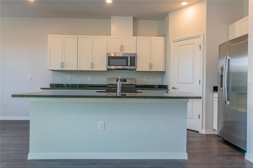 A kitchen features white cabinets, dark granite countertops, a central island, and stainless steel appliances — 1348 PALAU STREET SE, PALM BAY, FL