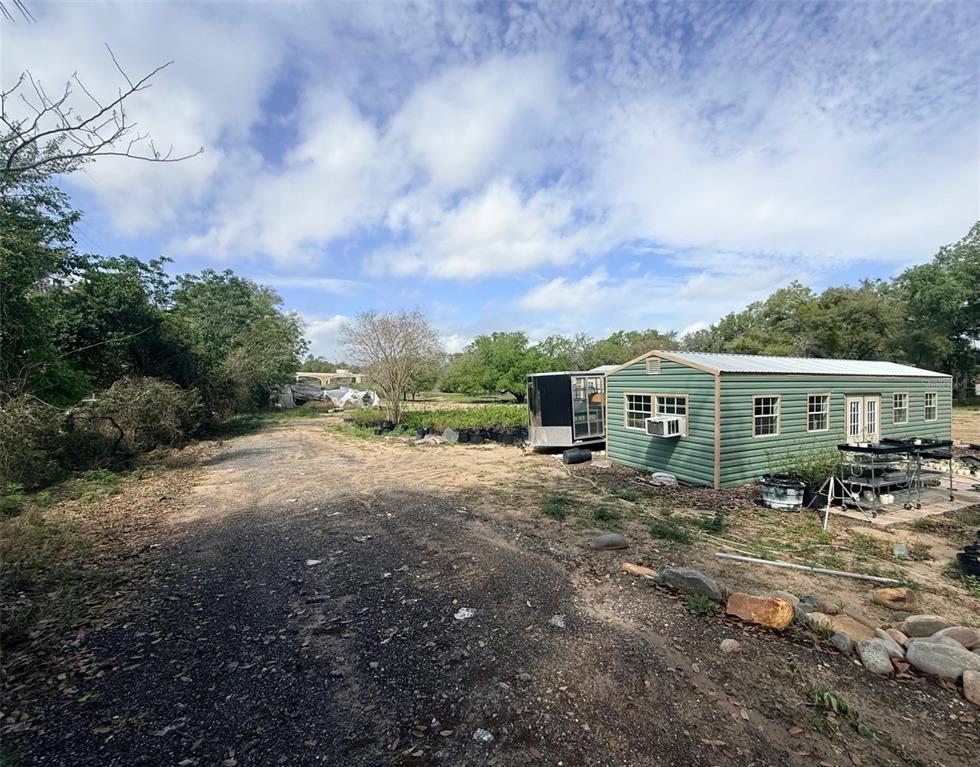 A green metal building sits on a dirt lot with a trailer and potted plants — 3330 PLYMOUTH SORRENTO ROAD, APOPKA, FL