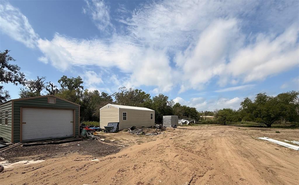 A dirt lot features a green metal garage, a beige shed, and a small trailer — 3330 PLYMOUTH SORRENTO ROAD, APOPKA, FL