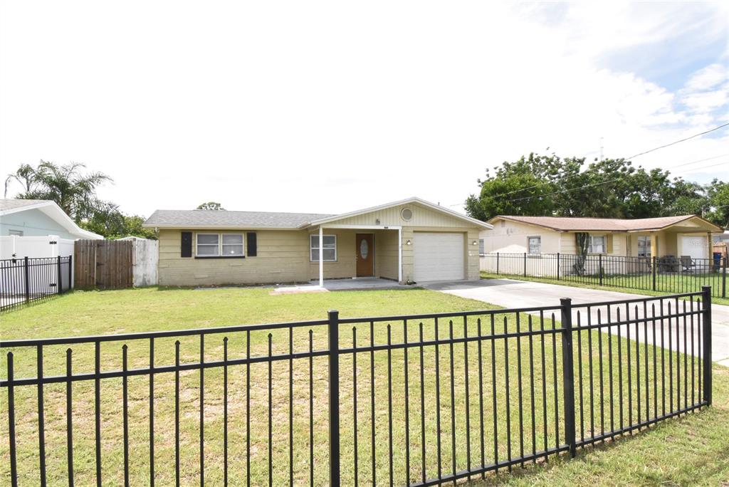 A single-story house with a tan exterior, a front-facing garage, and a black metal fence — 11025 PICKERING LANE, PORT RICHEY, FL