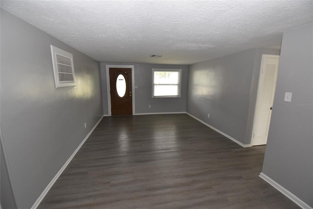 An empty room features gray walls, dark wood-look flooring, a front door, and a window — 11025 PICKERING LANE, PORT RICHEY, FL