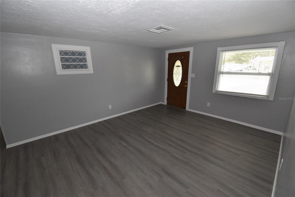 An empty room features gray walls, wood-look flooring, a front door, and a window — 11025 PICKERING LANE, PORT RICHEY, FL