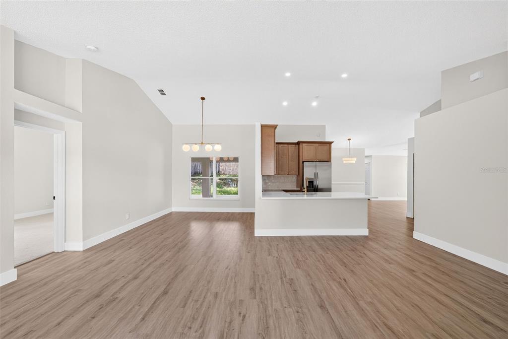 A bright living area with wood-look flooring, vaulted ceilings, and an adjacent kitchen with white countertops — 294 LAKE DOE BOULEVARD, APOPKA, FL