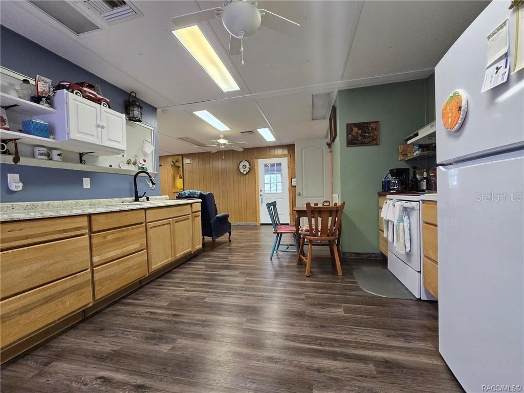 A kitchen with wood cabinets, light countertops, and wood-look flooring leads to a dining area — 10292 E PIKE DRIVE, INVERNESS, FL
