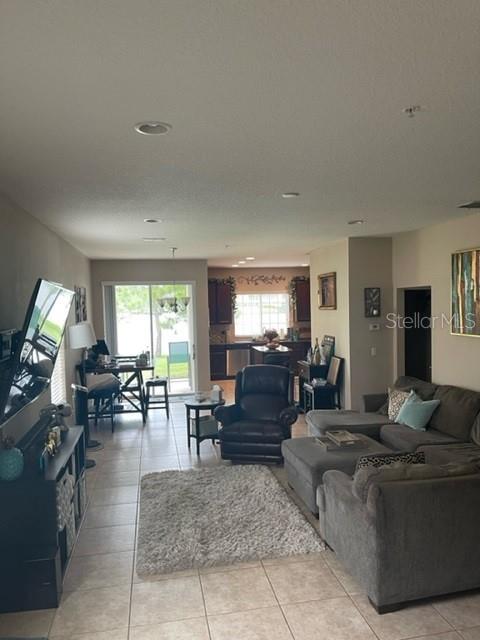 An open-concept living room features tile flooring, a gray sectional sofa, and a kitchen beyond — 2526 PASSAMONTE DRIVE UNIT 10F, WINTER PARK, FL