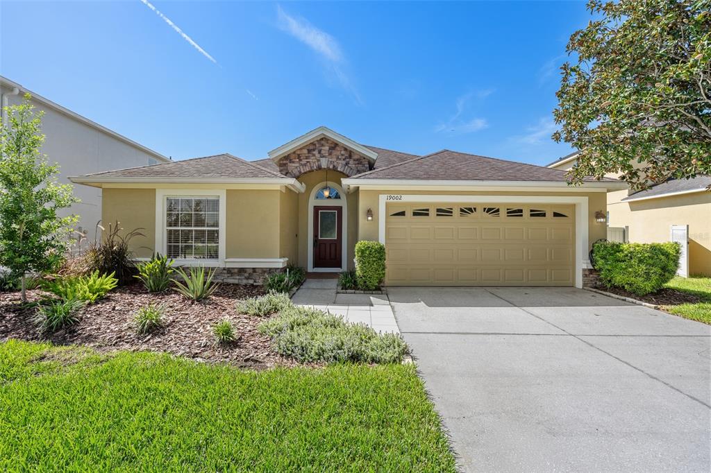 A single-story house with a tan stucco exterior, stone accents, and a two-car garage — 19002 NARIMORE DRIVE, LAND O LAKES, FL