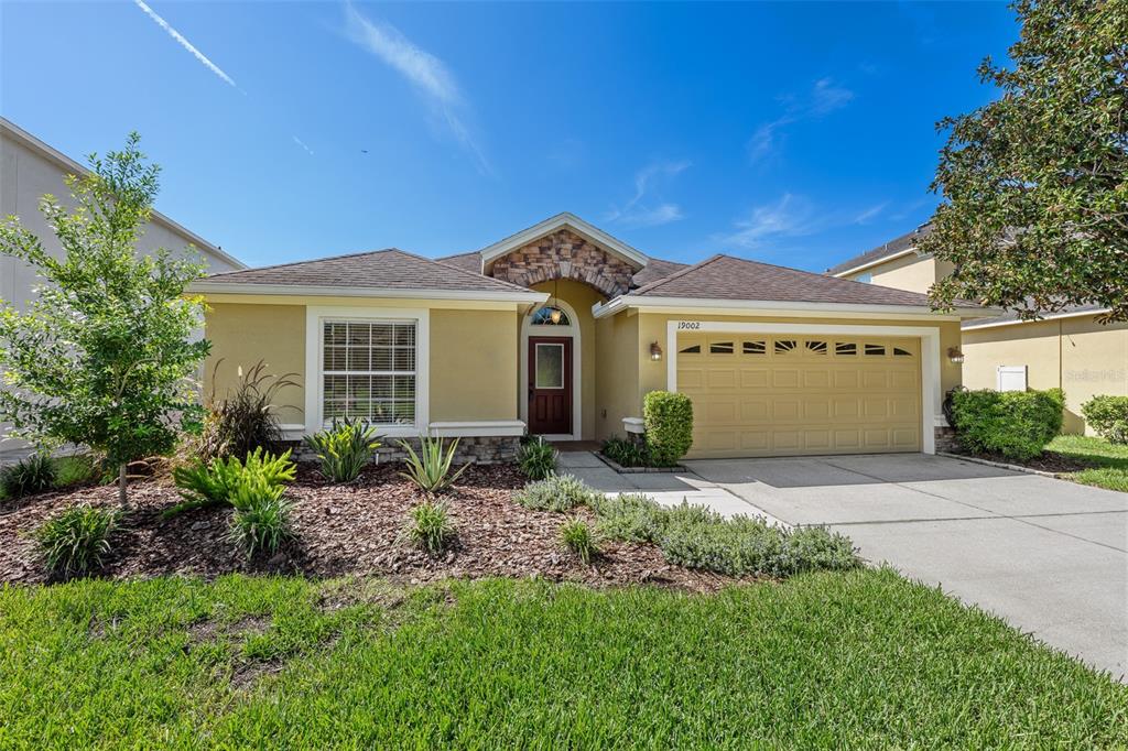 A single-story house with a tan stucco exterior, stone accents, and a two-car garage — 19002 NARIMORE DRIVE, LAND O LAKES, FL