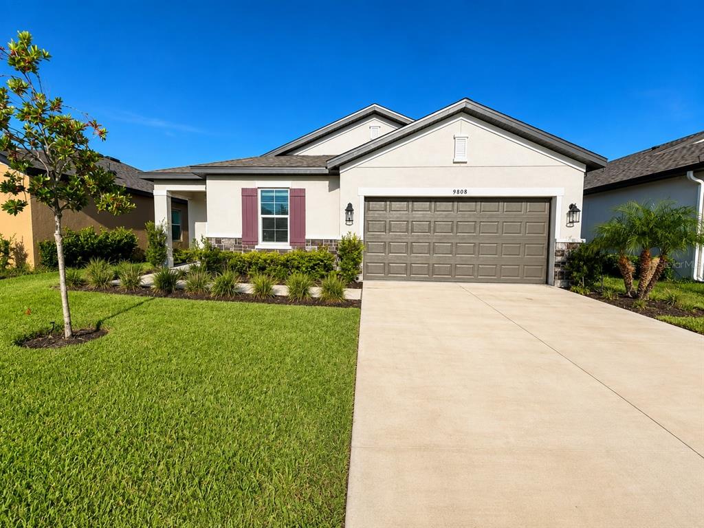 A single-story house with a beige stucco exterior, a two-car garage, and a landscaped lawn — 9808 LAST LIGHT GLEN, PARRISH, FL
