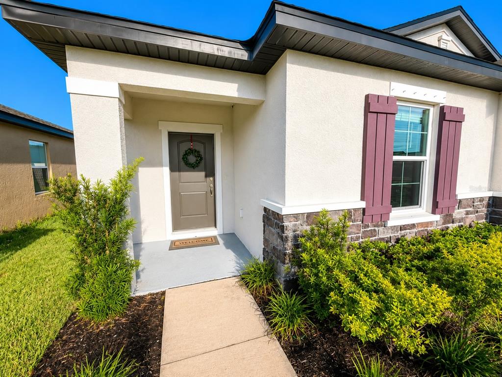 The exterior of a house features a tan front door, stone accents, and purple shutters — 9808 LAST LIGHT GLEN, PARRISH, FL
