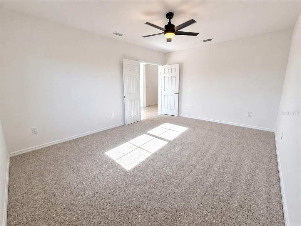 An empty bedroom features beige carpet, white walls, a ceiling fan, and open double doors — 9808 LAST LIGHT GLEN, PARRISH, FL