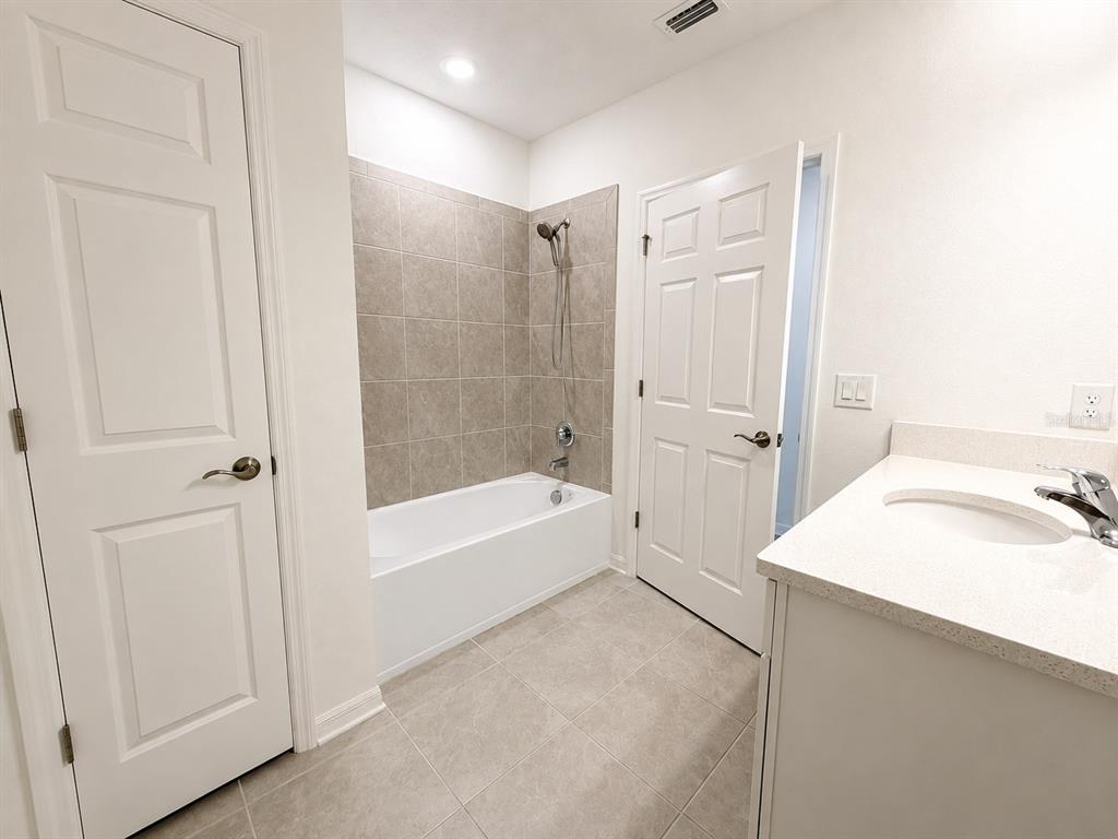 A bathroom features a white vanity, a tiled bathtub shower combo, and light-colored floor tiles — 9808 LAST LIGHT GLEN, PARRISH, FL