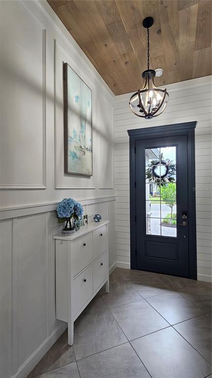 A foyer features a dark front door, white wall paneling, a wood-plank ceiling, and tile flooring — 5212 MARINA BASIN COURT, BRADENTON, FL