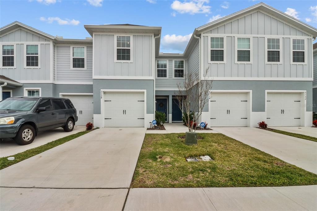 A row of three attached townhomes with gray siding, white garage doors, and concrete driveways — 3138 VICTORIA INLET DRIVE, HOLIDAY, FL